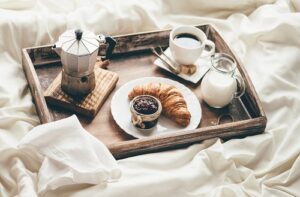 A photo showing a luxurious breakfast in bed with coffee and a croissant.