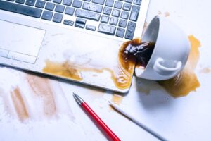 An image of an overturned coffee cup with coffee spilled on an expensive laptop.