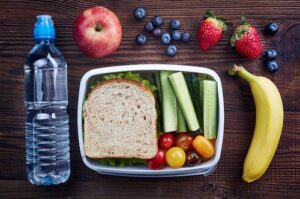 A photo showing a healthy packed lunch with water, sandwich, fruits and veggies.