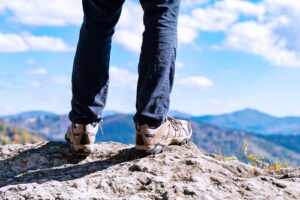 A photo showing the legs and feet of a hiker standing on the edge of a cliff.