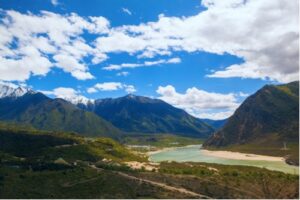 A photo showing a blue sky above mountains, plains and a river in Tibet.