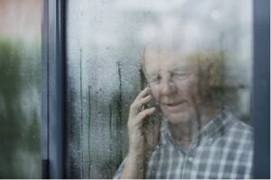 A photo showing a mature man looking out the window on a rainy day while talking on the phone.