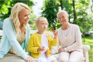 A photo showing a mother and grandmother with a young granddaughter blowing bubbles and enjoying time outside.