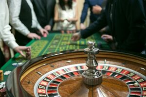 A casino roulette is shown in the foreground while people make bets in the background