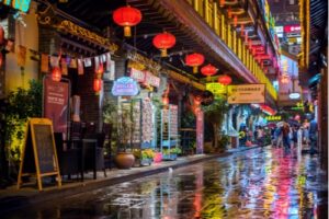 A photo showing businesses lining a street on a rainy night in Chongqing, China.