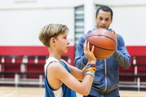 A photo showing a young boy being coached as he practices basketball.