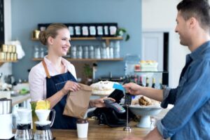 A photo of a barista and customer both smiling as the customer pays for his order.