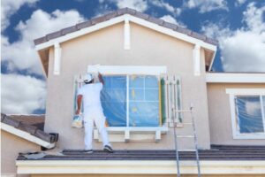 A photo showing a male house painter working on the exterior of a house.