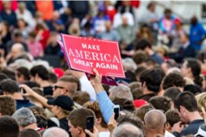 A photo showing the crowd at a Donald Trump rally with a person displaying a “Make America Great Again” sign.