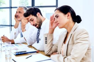 A photo showing three employees in a meeting with one looking frustrated and another yawning.