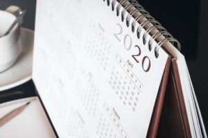 A photo showing a 2020 calendar sitting on a desk near papers and a cup of coffee.