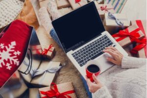 A photo showing a woman surrounded by gifts using her personal computer to do some holiday shopping.