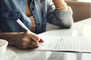 A photo of a woman seated at a table handwriting a letter.