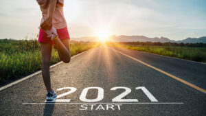 A runner stretches on an open road at a starting line marked “2021 start.”