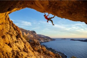 An image of a mountain climber dangling from a cliff’s edge with a view of mountains and water.