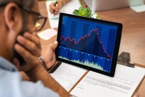 A photo showing a concerned man reviewing plummeting stock performance on a tablet screen.