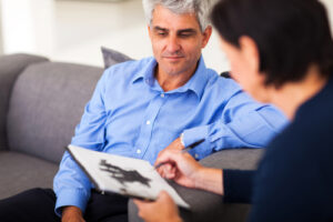 A photo of a therapist showing an older male patient a Rorschach test on a clipboard.