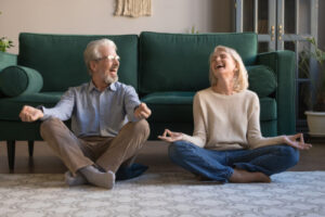 A photo showing a senior couple practicing yoga together and laughing.