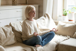 A photo of a mature woman sitting on her couch meditating.