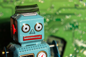 A photo of a vintage toy robot in front of a computer circuit board background.