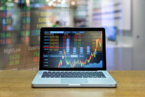 A photo showing a computer on a table with stock market charts and ticker overlays.