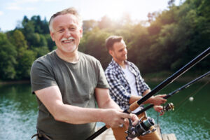 A photo of a smiling older man fishing with a younger man off a dock.