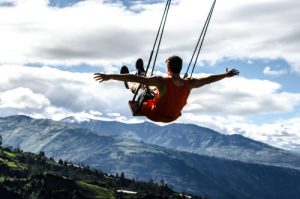 A photo of a man on a swing overlooking a landscape of mountains and trees.