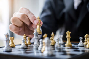 A photo showing a well-dressed man’s hand moving a chess piece on a chessboard.