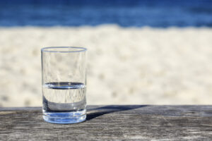 A photo showing a glass half-full of water in front of an ocean background.