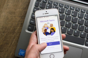 A photo showing a hand holding an iPhone with the Microsoft Teams app open.