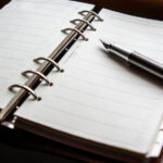 A photo of a pen resting on a binder-spine notebook.