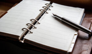 A photo of a pen resting on a binder-spine notebook.