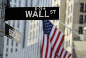 A photo of a street sign for Wall Street with the American flag in the background.