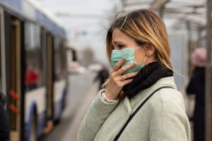 A woman wears a mask while waiting for the bus