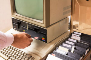 A man inserts a floppy disk into an old Apple computer