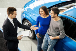 A photo showing a salesman at a car dealership talking to a young couple.