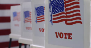 row of voting booths showing signs with the word “Vote” and the American flag.