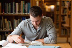 A photo showing a young man studying a book in a library.