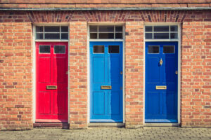 Three differently coloured front doors at the entrance of old English terraced houses.