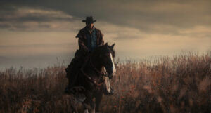 A photo of a cowboy riding his horse through a field at dusk.