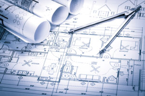 A photo showing rolls of architecture blueprints and a drawing compass on a table.