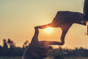 A photo of a person’s hands making a rectangle in front of a sunset.