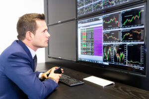 A photo of a stockbroker seated at a trading desk analyzing multiple stock charts on computer screens.