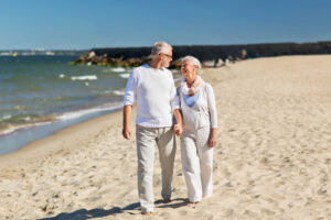 An image of a senior couple holding hands as they walk happily along a beach by themselves.