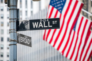 A photo showing the Wall Street sign in front of a background of American flags.