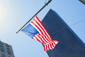 A photo of an American flag blowing in the wind in front of tall skyscrapers.