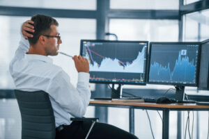 A photo showing a stock trader analyzing multiple computer screens with stock charts.