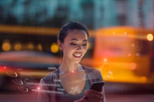 A photo showing a young woman using her iPhone with blurred lights from fast-moving cars behind her.