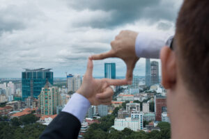 A photo showing a businessman make a frame with his hands looking through at a city skyline.