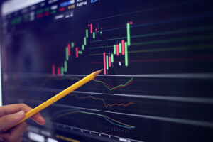 A photo of the hand of an investment analysis holding a pencil to a technical chart pattern